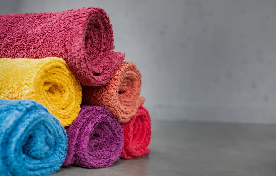 Opgerolde badhanddoeken in fuchsia, geel, blauw en roze. Badtextiel van Abyss & Habidecor.