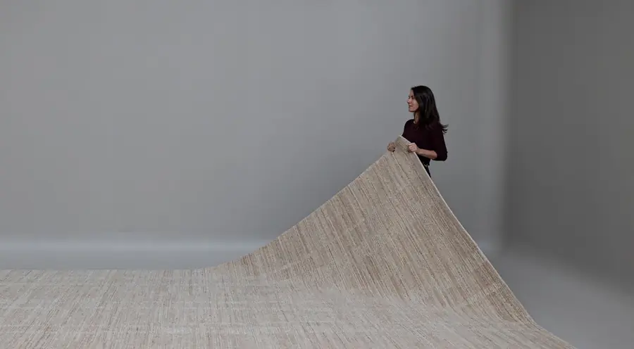 Een groot tapijt wordt uitgerold in het atelier. Tapijt van Ancré rugs.
