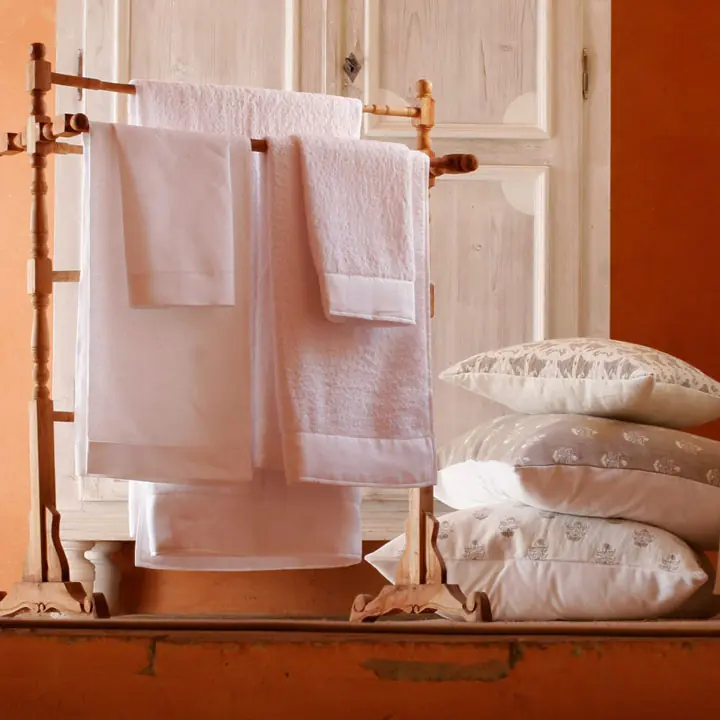 Badtextiel op een rek bij een oranje wand. Stoffen van C&C Milano.