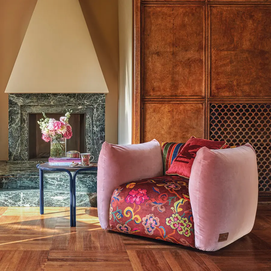 Roze fluwelen fauteuil met bloemenzitting bij een marmeren haard. Stoffen van Etro.