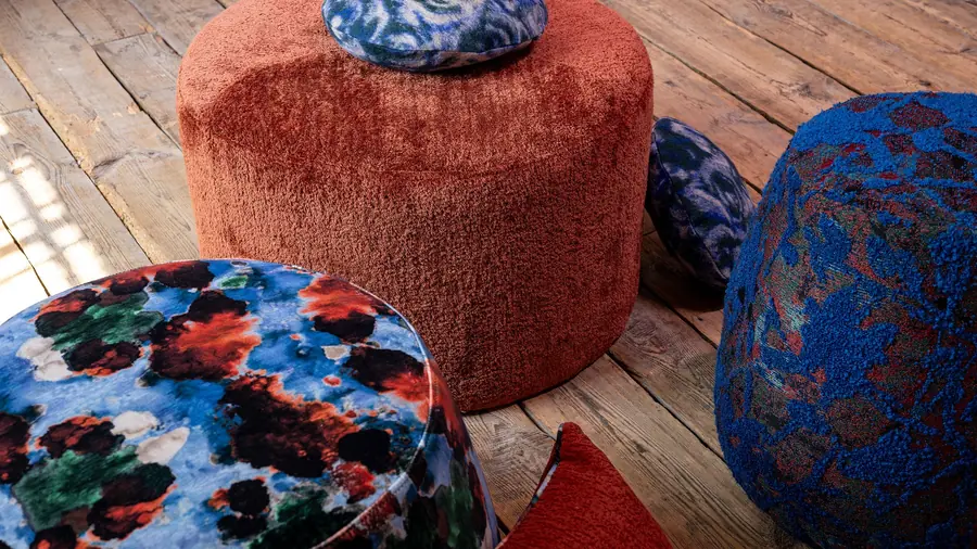 Poefen in roestrode en blauwe chenille met een gebloemd kussen. Stoffen van Fine.