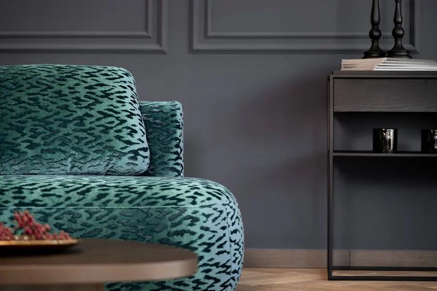 Fauteuil in turquoise luipaardvelours tegen een donkergrijze lambrisering. Stoffen van Fine.