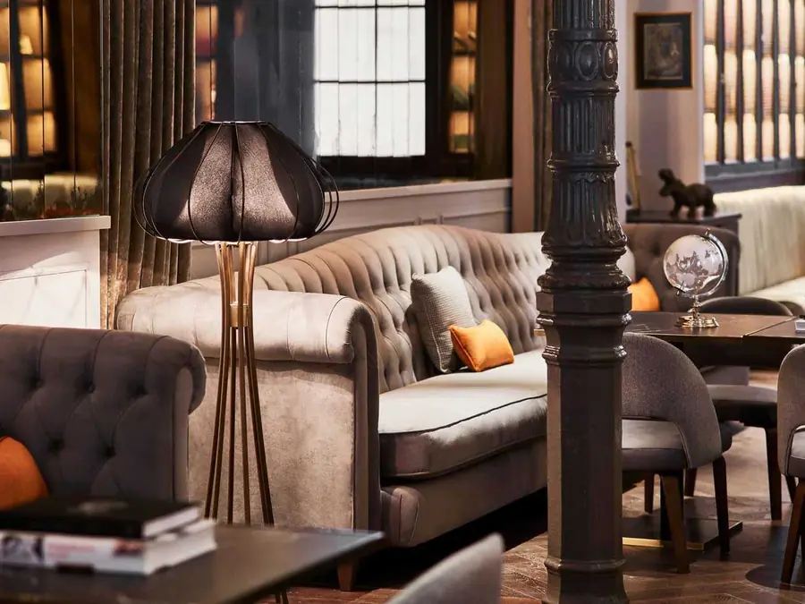 Lederen chesterfield met oranje kussen bij een staande lamp. Stoffen van Gastón y Daniela.