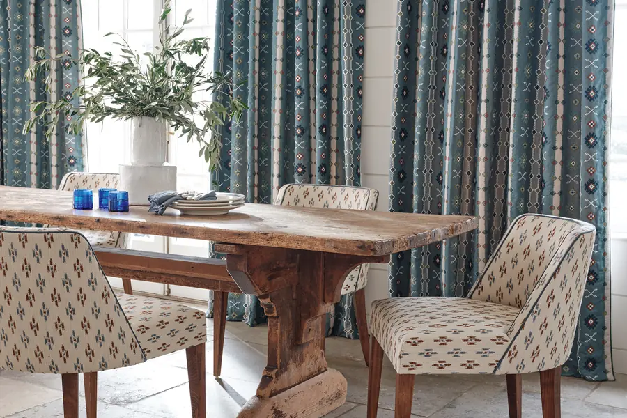 Eetkamer met blauwe ikatgordijnen en bedrukte stoelen. Stoffen van Jane Churchill.