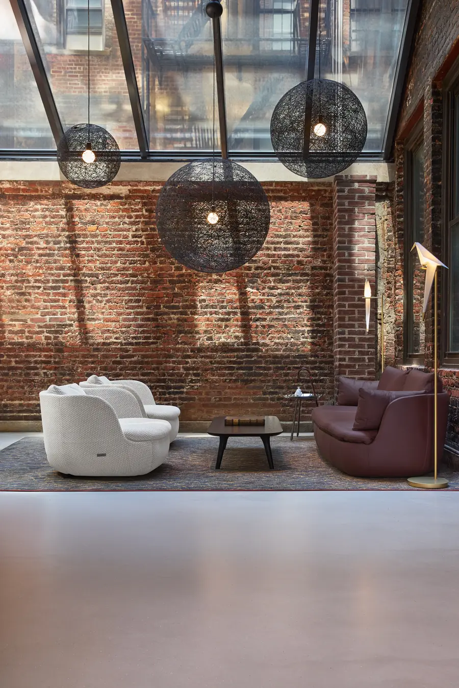 Loft met bakstenen muur, hanglampen en witte fauteuils. Meubelen van Moooi.
