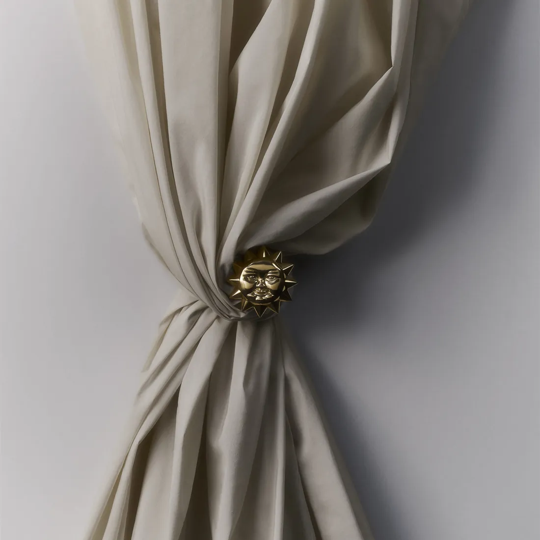 Beige gordijn bijeengehouden met een goudkleurige embrasse. Stoffen van Sahco.