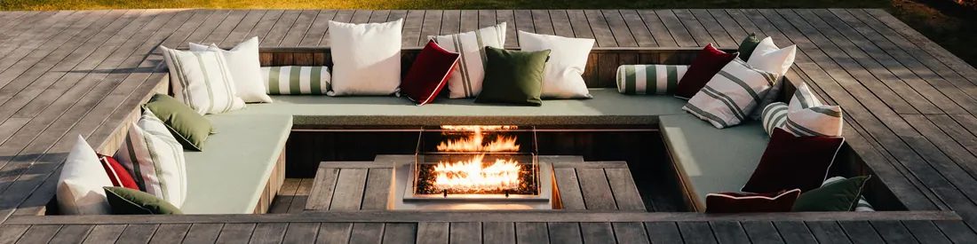 Terras met loungebanken en kussens rond een vuurtafel. Stoffen van Sunbrella.